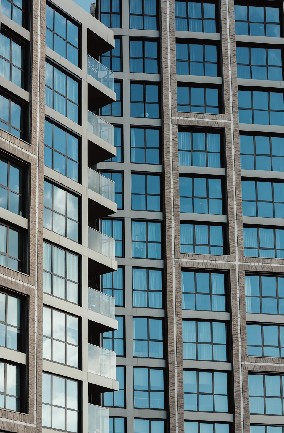 Illustrative photograph: Tall residential facade with a grid of windows and projecting glass balconies