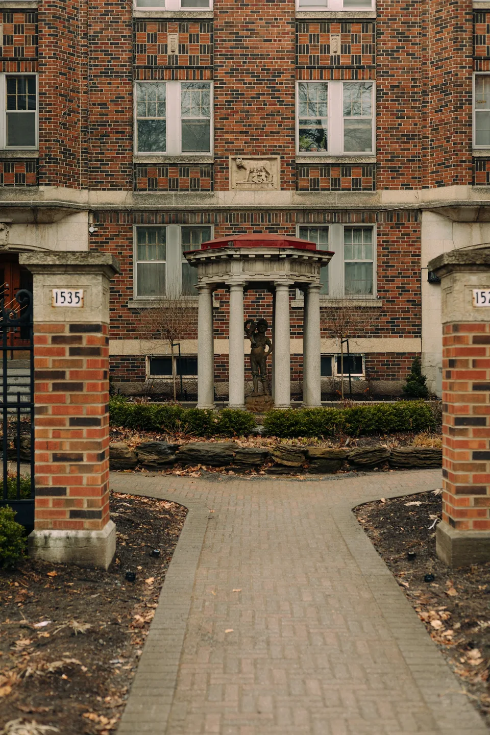 Illustrative photograph: Brick residential entrance with paired doors and a paved approach between brick columns
